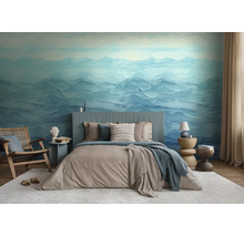 Fotobehang met blauw bergmotief in aquarellook in een slaapkamer met modern tweepersoonsbed, houten stoel en licht tapijt.