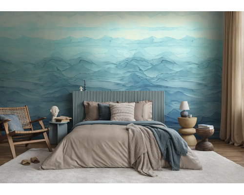 Fotobehang met blauw bergmotief in aquarellook in een slaapkamer met modern tweepersoonsbed, houten stoel en licht tapijt.
