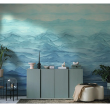 Moderne woonkamer met fotobehang met blauw bergmotief in aquarelstijl. Minimalistisch dressoir met decoratie en kamerplanten.