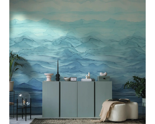 Moderne woonkamer met fotobehang met blauw bergmotief in aquarelstijl. Minimalistisch dressoir met decoratie en kamerplanten.