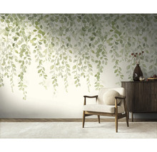 Fotobehang met hangende groene bladeren in aquarelstijl in een licht ingerichte woonkamer met fauteuil en dressoir.
