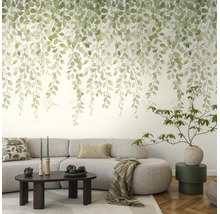 Fotobehang met hangende groene bladeren in aquarelstijl in een lichte woonkamer met grijze bank.