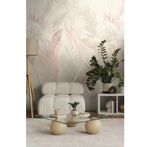Moderne woonkamer met behang met tropisch bladpatroon, een zachte witte fauteuil, glazen salontafel en een houten driepoot vloerlamp.