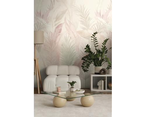 Moderne woonkamer met behang met tropisch bladpatroon, een zachte witte fauteuil, glazen salontafel en een houten driepoot vloerlamp.