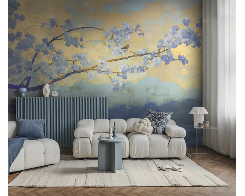 Vliesbehang met bloesemtak en vogel in een moderne woonkamer met een witte modulaire bank en blauw wandpaneel.