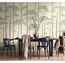 Vliesbehang met gestileerd bosmotief van hoge boomstammen en groene kruinen in een lichte eetkamer met houten tafel en stoelen.