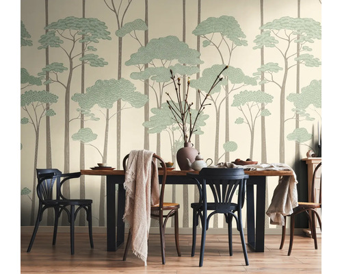 Vliesbehang met gestileerd bosmotief van hoge boomstammen en groene kruinen in een lichte eetkamer met houten tafel en stoelen.