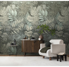 Vliesbehang met een groot, tropisch bladerpatroon in gedempte groentinten in een modern ingerichte woonkamer met dressoir en fauteuil.