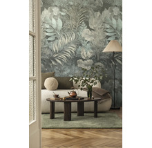 Vliesbehang met botanisch bladmotief in een woonkamer met een lichte bank, een donkere salontafel, een vloerlamp en een groen vloerkleed.