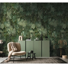 Vliesbehang met jungle-motief van monstera- en palmbladeren in een moderne woonkamer met groen dressoir en beige fauteuil.