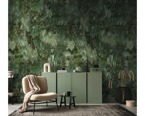 Vliesbehang met jungle-motief van monstera- en palmbladeren in een moderne woonkamer met groen dressoir en beige fauteuil.