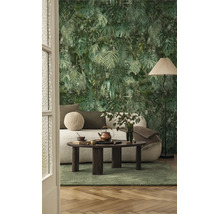 Vliesbehang met jungle-motief van palmbladeren en monstera in een woonkamer met een lichte bank, donkere houten tafel en een groen tapijt.