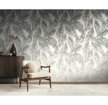Lichte woonkamer met een groot fotobehang met bladerdessin, een houten fauteuil met stoffen bekleding en een donker houten dressoir.