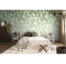 Lichte slaapkamer met fotobehang met grote groene bladeren, een bed met kussens, witte nachtkastjes en diverse kamerplanten.