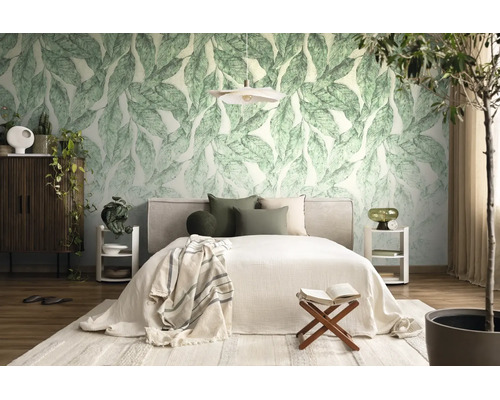 Lichte slaapkamer met fotobehang met grote groene bladeren, een bed met kussens, witte nachtkastjes en diverse kamerplanten.