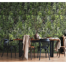 Eetkamer met botanisch behang met een dicht groen blader- en plantenpatroon voor een houten eettafel met stoelen.