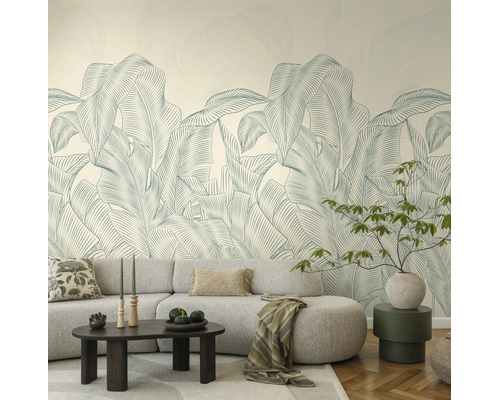 Vliesbehang met groot palmbladpatroon in een licht ingerichte woonkamer met een grijze bank en salontafel.