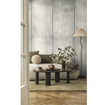 Woonkamer met wandpanelen in betonlook, een lichte bank, een donkerhouten salontafel en een vloerlamp met geplooide kap.