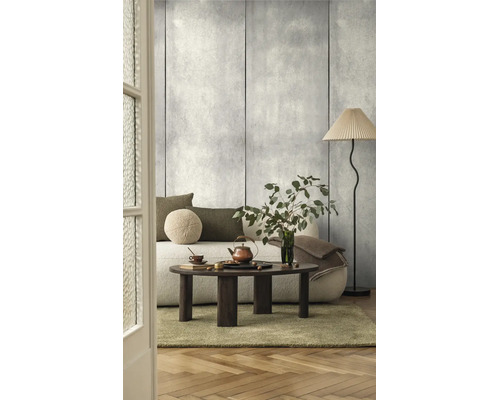 Woonkamer met wandpanelen in betonlook, een lichte bank, een donkerhouten salontafel en een vloerlamp met geplooide kap.