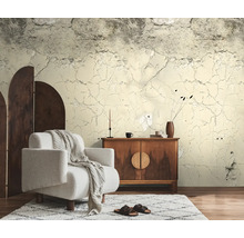 Fotobehang met beton- en gebarsten pleisterlook in een woonkamer met een witte fauteuil en een houten dressoir.