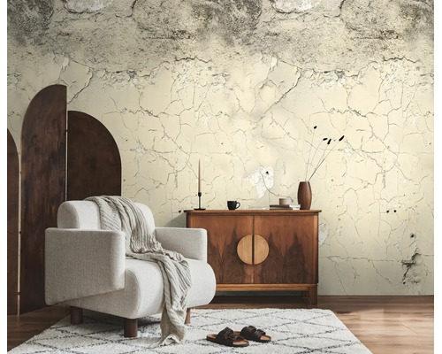 Fotobehang met beton- en gebarsten pleisterlook in een woonkamer met een witte fauteuil en een houten dressoir.