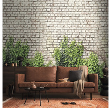Fotobehang met bakstenen muur en groene klimop achter een bruine leren bank in een modern ingerichte woonkamer.