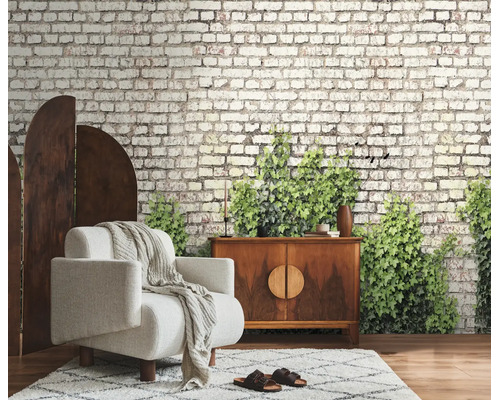 Fotobehang met baksteenlook en groene klimop in een woonkamer met fauteuil en dressoir.
