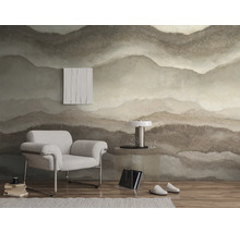 Vliesbehang met abstract bergmotief in natuurlijke aardetinten in een moderne woonkamer met fauteuil en bijzettafel.