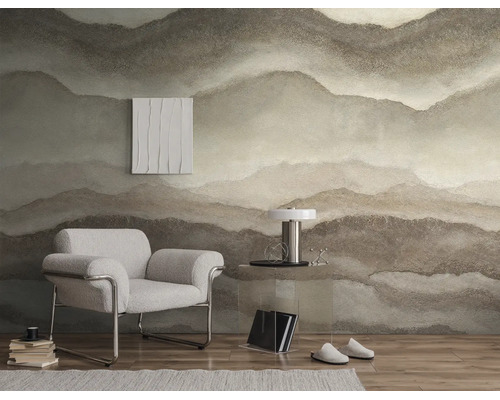 Vliesbehang met abstract bergmotief in natuurlijke aardetinten in een moderne woonkamer met fauteuil en bijzettafel.