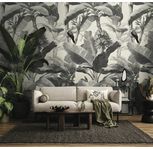 Woonkamer met zwart-wit fotobehang in jungle-ontwerp met bananenbladeren en vogels, lichte bank, houten tafel en kamerplanten.
