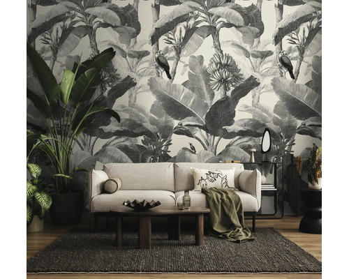 Woonkamer met zwart-wit fotobehang in jungle-ontwerp met bananenbladeren en vogels, lichte bank, houten tafel en kamerplanten.