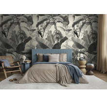 Lichte slaapkamer met botanisch fotobehang met bananenbladeren en vogels in vintage stijl achter een blauw bed.