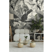 Vliesbehang met zwart-wit jungle-ontwerp met bladeren en vogels in een modern ingerichte woonkamer met lichte fauteuil.