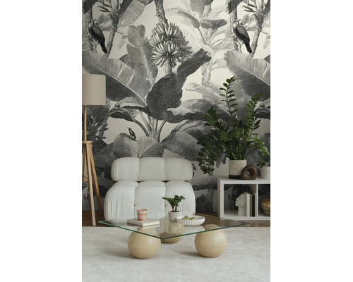 Vliesbehang met zwart-wit jungle-ontwerp met bladeren en vogels in een modern ingerichte woonkamer met lichte fauteuil.