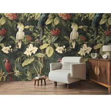Fotobehang met jungle-thema, papegaaien en tropische bloemen achter een lichte fauteuil en een houten kast in een woonkamer.