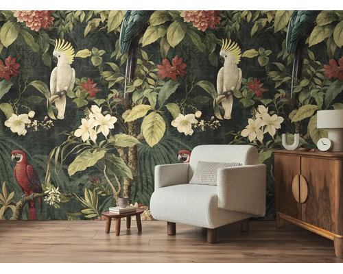 Fotobehang met jungle-thema, papegaaien en tropische bloemen achter een lichte fauteuil en een houten kast in een woonkamer.