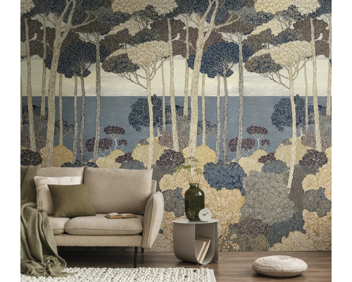 Vliesbehang met bosmotief, gestileerde pijnbomen en struiken in natuurtinten, woonkamer met beige bank en bijzettafel.