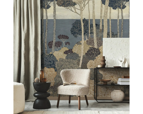 Vliesbehang met gestileerd bosmotief van dennen en struiken in blauw- en beigetinten achter een lichte fauteuil in een moderne kamer.