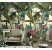 Fotobehang met tropisch motief van bananenbladeren en witte en roze bloemen achter een lichte bank in de woonkamer.