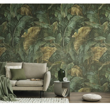 Vliesbehang met een groot junglepatroon van groene en bruine bladeren achter een beige bank in een woonkamer.
