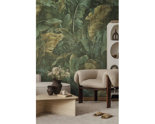 Vliesbehang met grote botanische bladeren in een modern ingerichte woonkamer met fauteuil en salontafel.