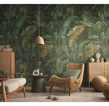 Vliesbehang met een groot tropisch bananenbladpatroon in een woonkamer met een rotan fauteuil en houten dressoir.