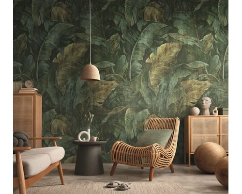 Vliesbehang met een groot tropisch bananenbladpatroon in een woonkamer met een rotan fauteuil en houten dressoir.