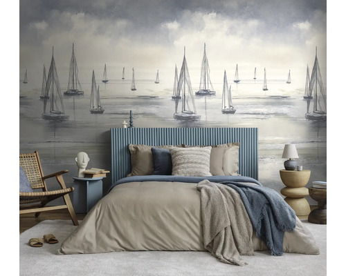 Slaapkamer met fotobehang van zeilboten, bed met blauw geribbeld hoofdbord en beddengoed in neutrale tinten, houten stoel en moderne bijzettafels.