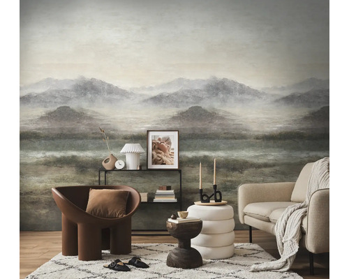 Wandvullend fotobehang met bergmotief in een woonkamer met fauteuil, bank, vloerkleed en decoratie op een plank.