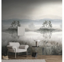 Fotobehang met een mistig berglandschap, bomen en een meer in een moderne woonkamer met een grijze fauteuil en houten vloer.