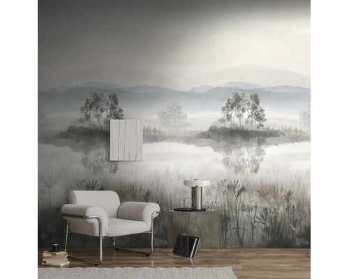 Fotobehang met een mistig berglandschap, bomen en een meer in een moderne woonkamer met een grijze fauteuil en houten vloer.