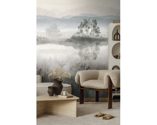 Moderne, lichte woonkamer met vliesfotobehang met mistig berglandschap, een fauteuil van stof en een salontafel van hout.