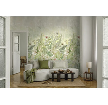 Woonkamer met botanisch behang met varens en bladeren. Een lichte bank met kussens en deken staat voor de wand op een natuurlijk kleed.