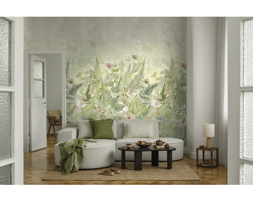 Woonkamer met botanisch behang met varens en bladeren. Een lichte bank met kussens en deken staat voor de wand op een natuurlijk kleed.